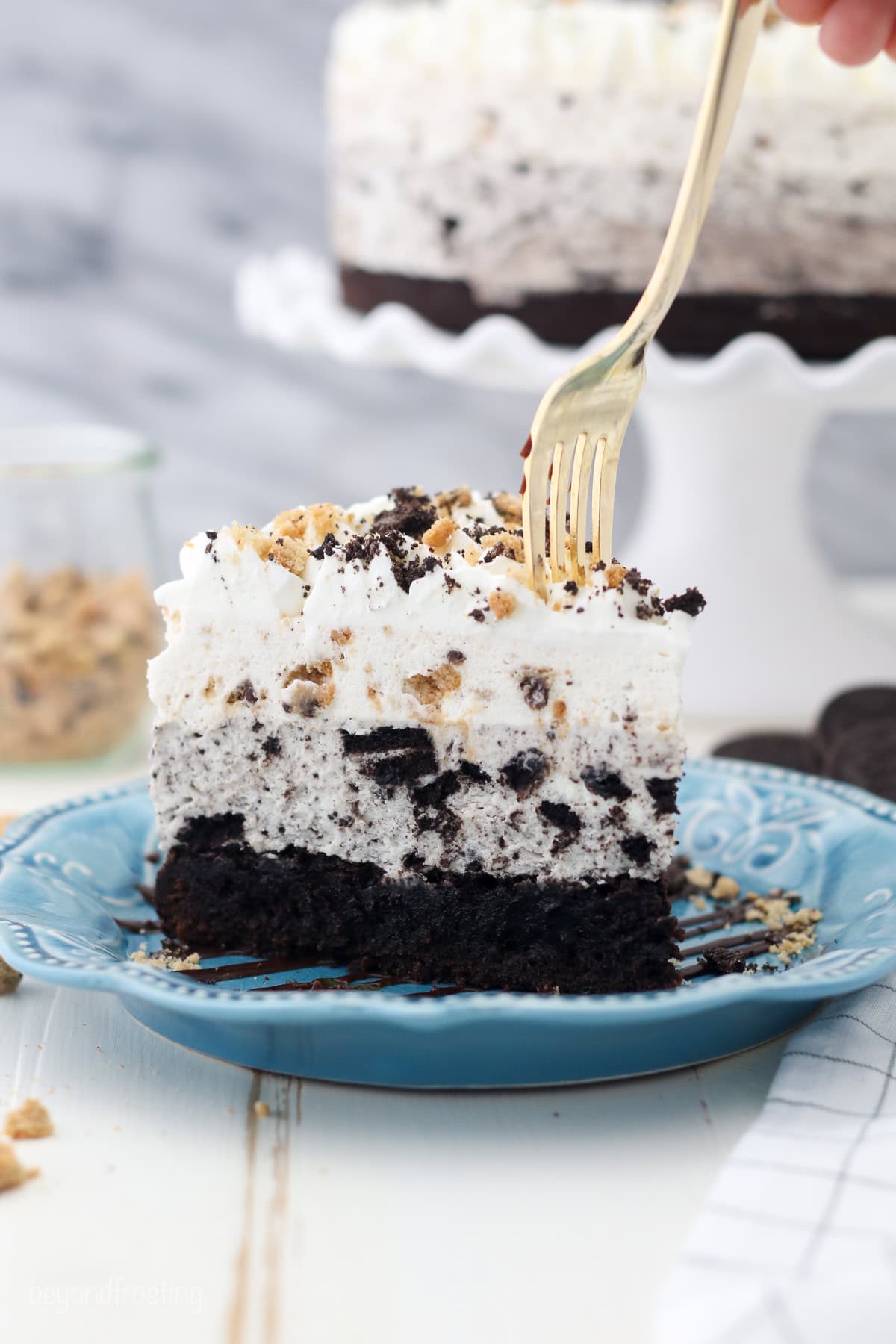 A fork stuck into a slice of Oreo brookie mousse cake on a blue plate.