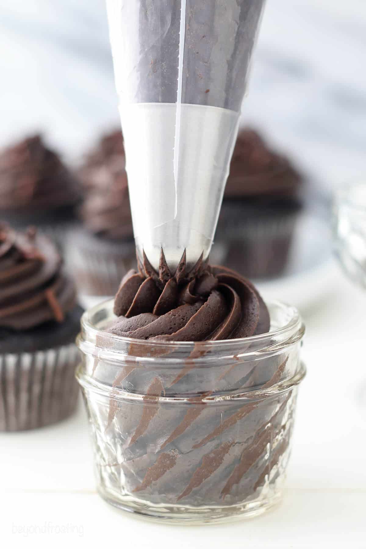 A piping tip pipes chocolate frosting into a glass jar.