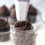 A large piping bag piping chocolate frosting into a small glass jar.