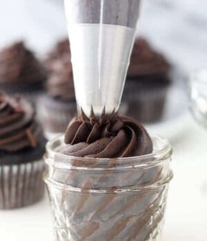 A large piping bag piping chocolate frosting into a small glass jar.