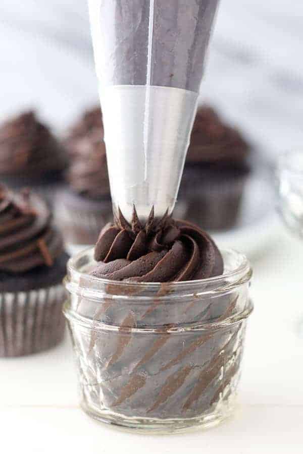 A large piping bag piping chocolate frosting into a small glass jar.