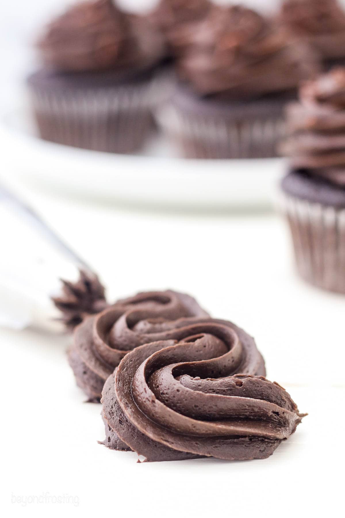 A piping tip pipes a squiggle of chocolate frosting onto a countertop.