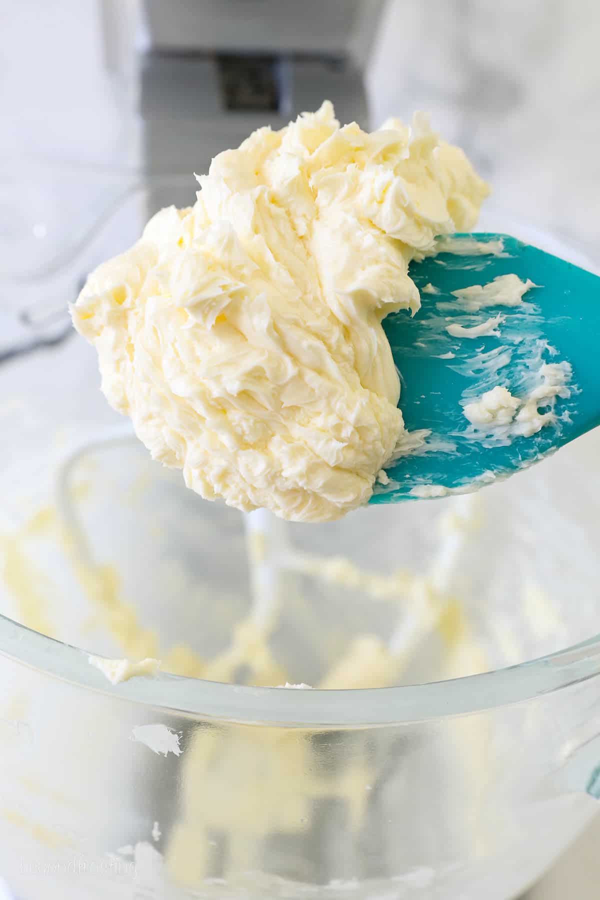 Beaten cold butter lifted from a mixing bowl with a blue spoon.