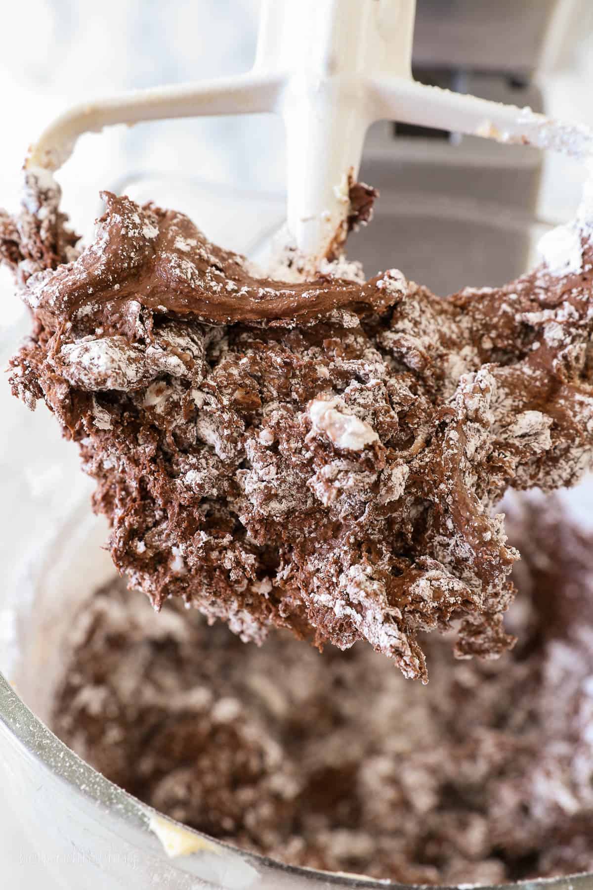 A stand mixer attachment coated in partially mixed chocolate frosting and powdered sugar.