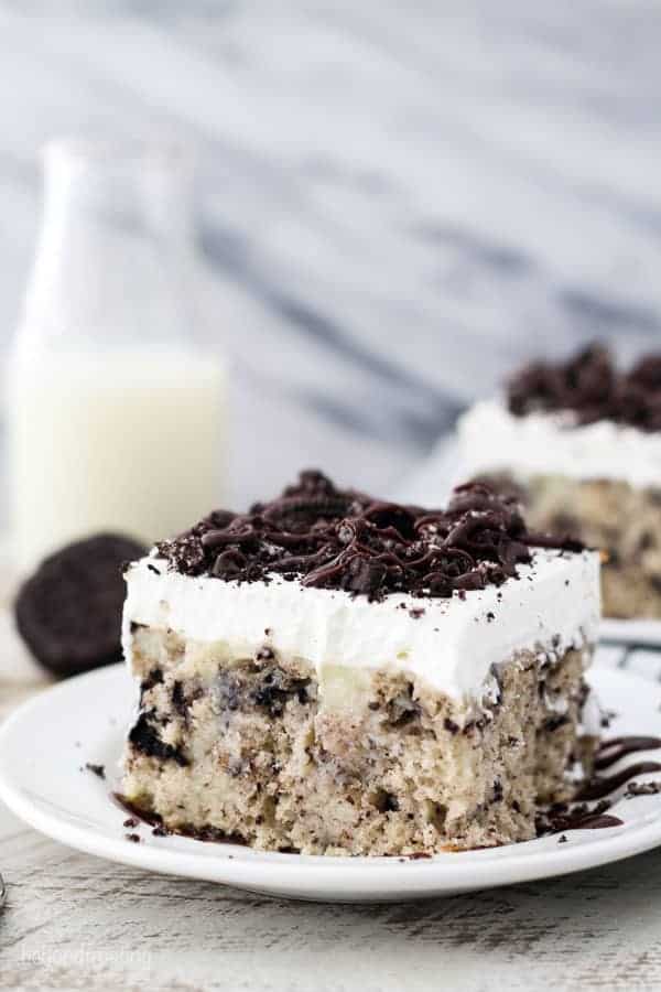 A white plate with a slice of Oreo Cake loaded with Oreo cookies and topped with whipped cream.