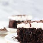 A close up shot of a slice of dark chocolate cake with whipped cream and hot fudge on top