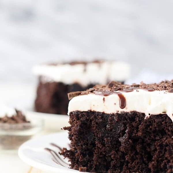 Close up of a slice of chocolate poke cake topped with whipped cream and chocolate sauce.