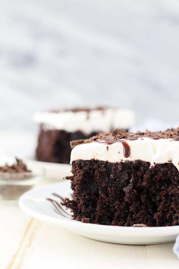 A close up shot of a slice of dark chocolate cake with whipped cream and hot fudge on top