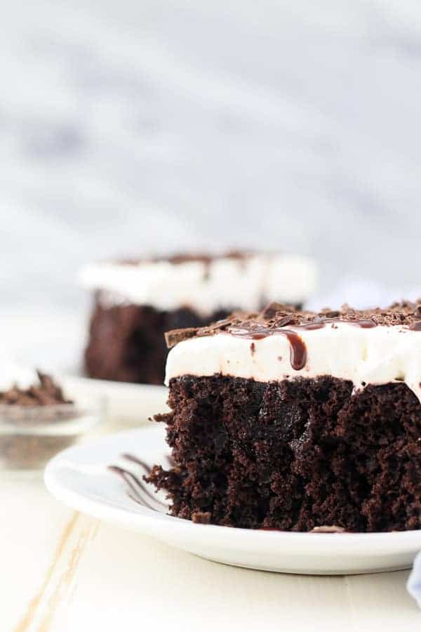 Close up of a slice of chocolate poke cake topped with whipped cream and chocolate sauce.