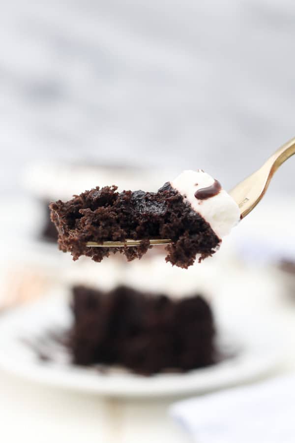 Close up of a gold fork holding up a big bite of chocolate poke cake.