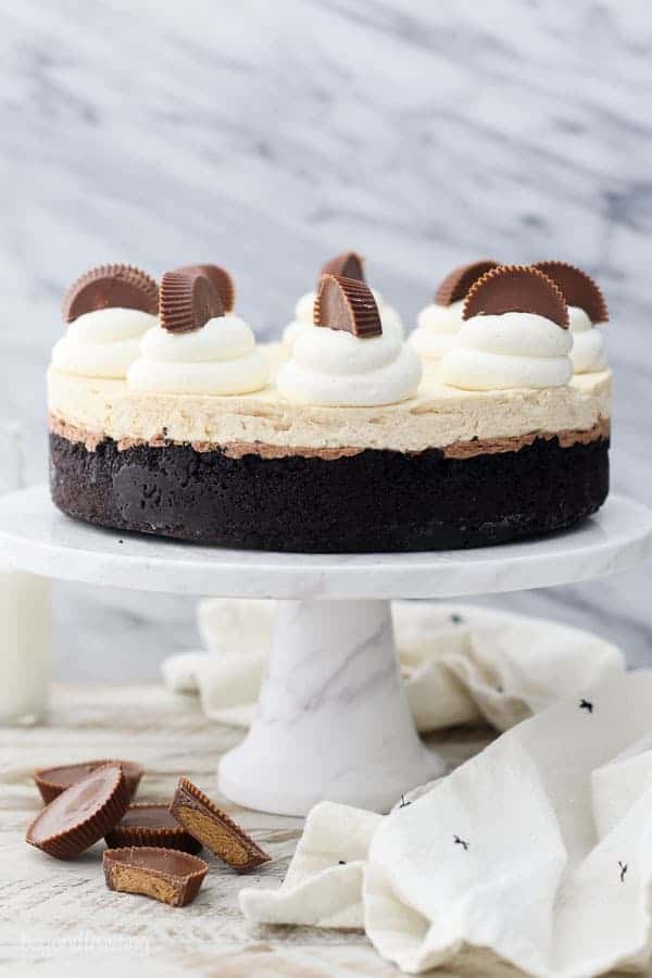 A gorgeous photo of a double layer peanut butter chocolate mousse pie on a marble cake stand styled with Reese's peanut butter cups and whipped cream