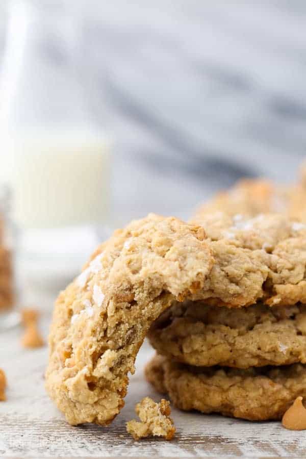 An oatmeal cookie with a big bite taken out of it is leaning against a stack of cookies