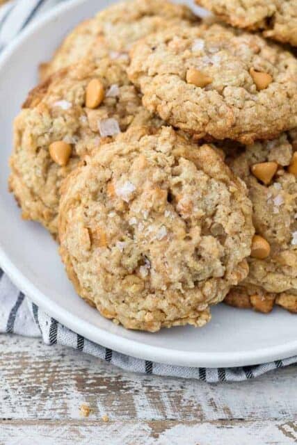 A white rimmed plate with stacks of butterscotch oatmeal cookies sprinkled with flakey sea salt