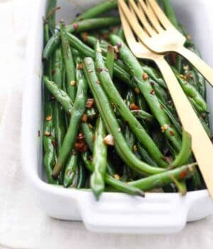 A small casserole dish filled with green beans and 2 gold forks.