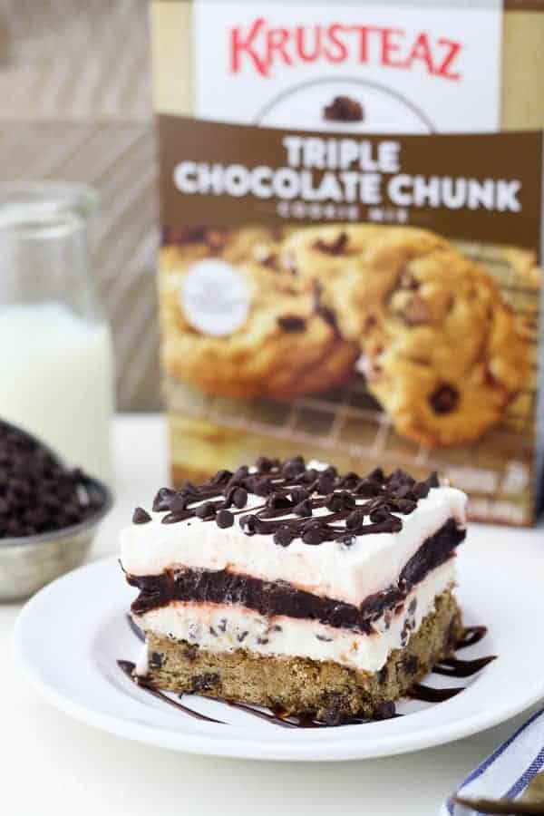 A plate with a big slice of chocolate chip cookie layered desserts and a box of cookie mix in the background