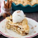 A piece of apple pie on a plate with ice cream on top and the remaining pie in the background