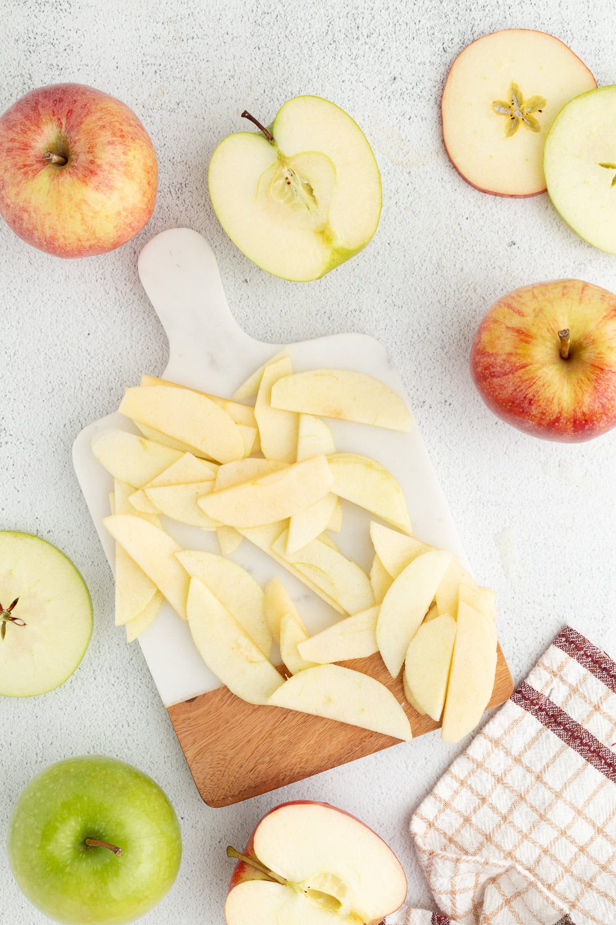 Overhead view of apple slices on a cutting board surrounded by uncut apples.