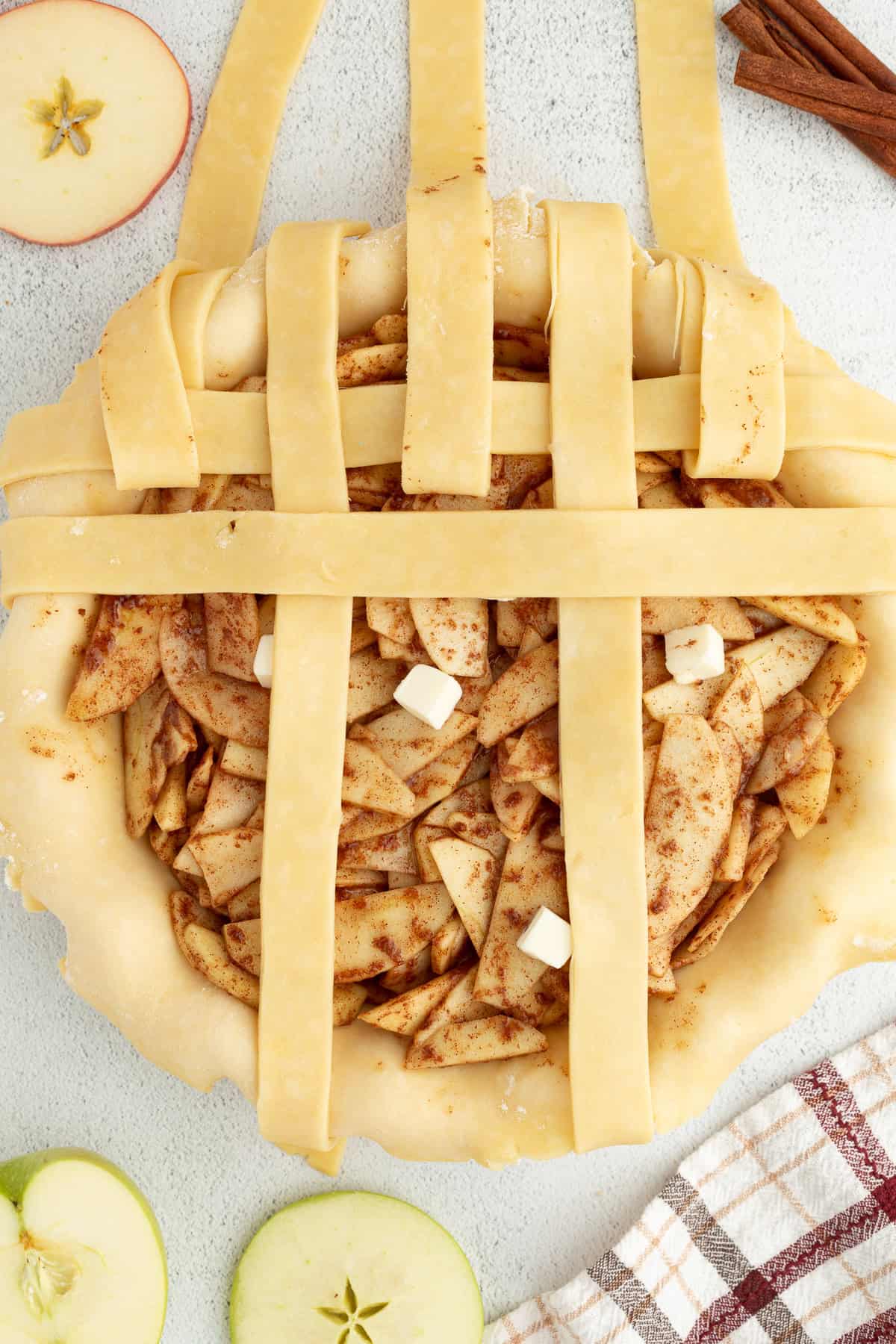 Partially woven dough strips on top of a filled apple pie.