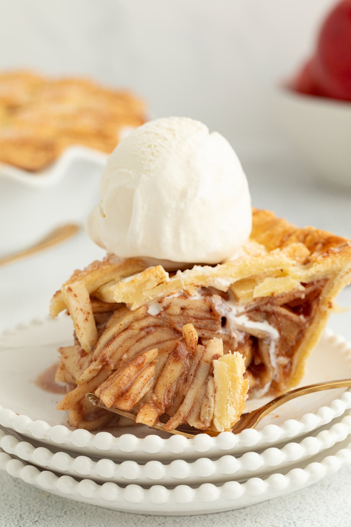 A forkful of apple pie next to a slice topped with ice cream on a plate.