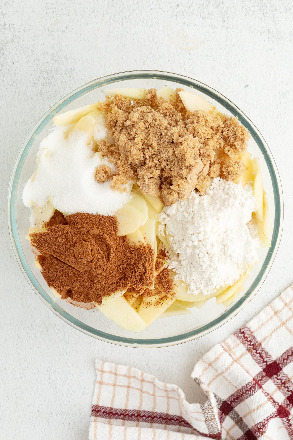 Sliced apples, sugar, cinnamon, and flour combined in a bowl.