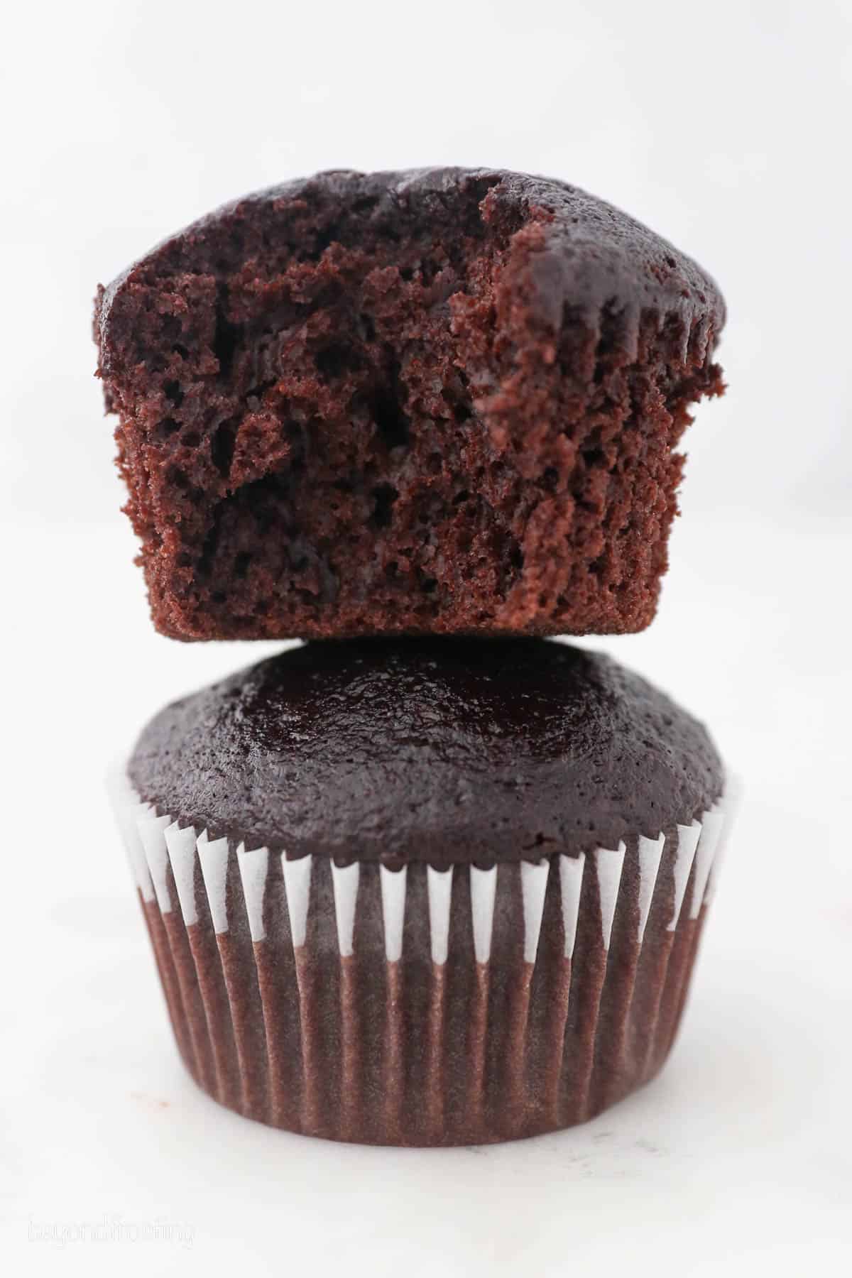 Two chocolate cupcakes stacked on top of one another, with a bite missing from the top cupcake.