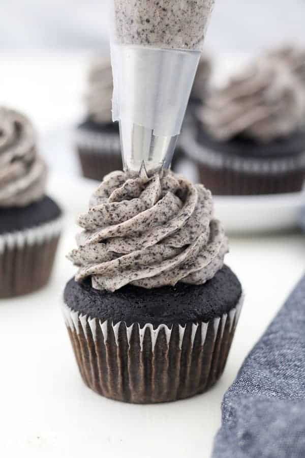 A piping bag filled with Oreo buttercream is piping a chocolate cupcake