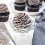 A glass dessert bowl filled with pipped Oreo Frosting and there are frosted cupcakes in the background