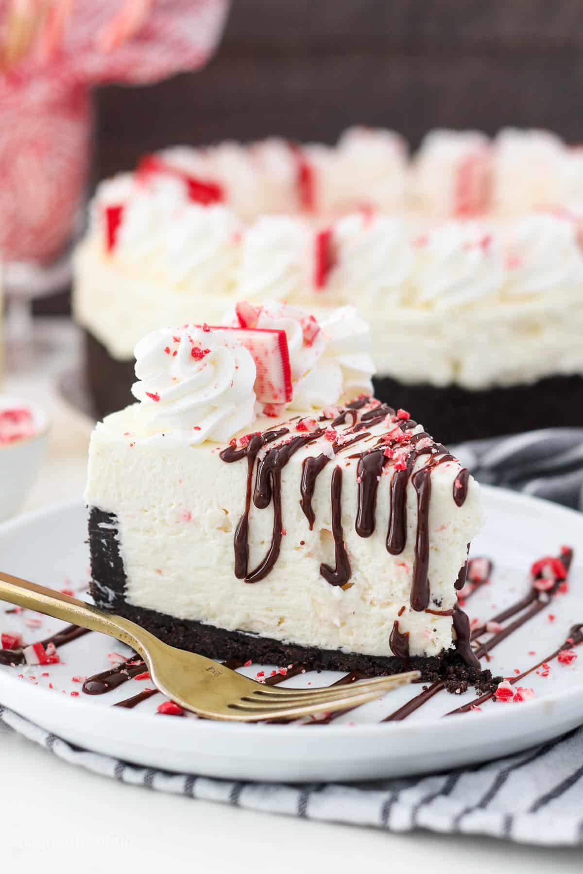 A gorgeous tall slice of a peppermint cheesecake on a white round plate with a gold fork