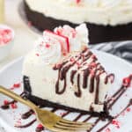 An overhead shot of a slice of white chocolate cheesecake with drizzles of fudge on top and peppermint candy