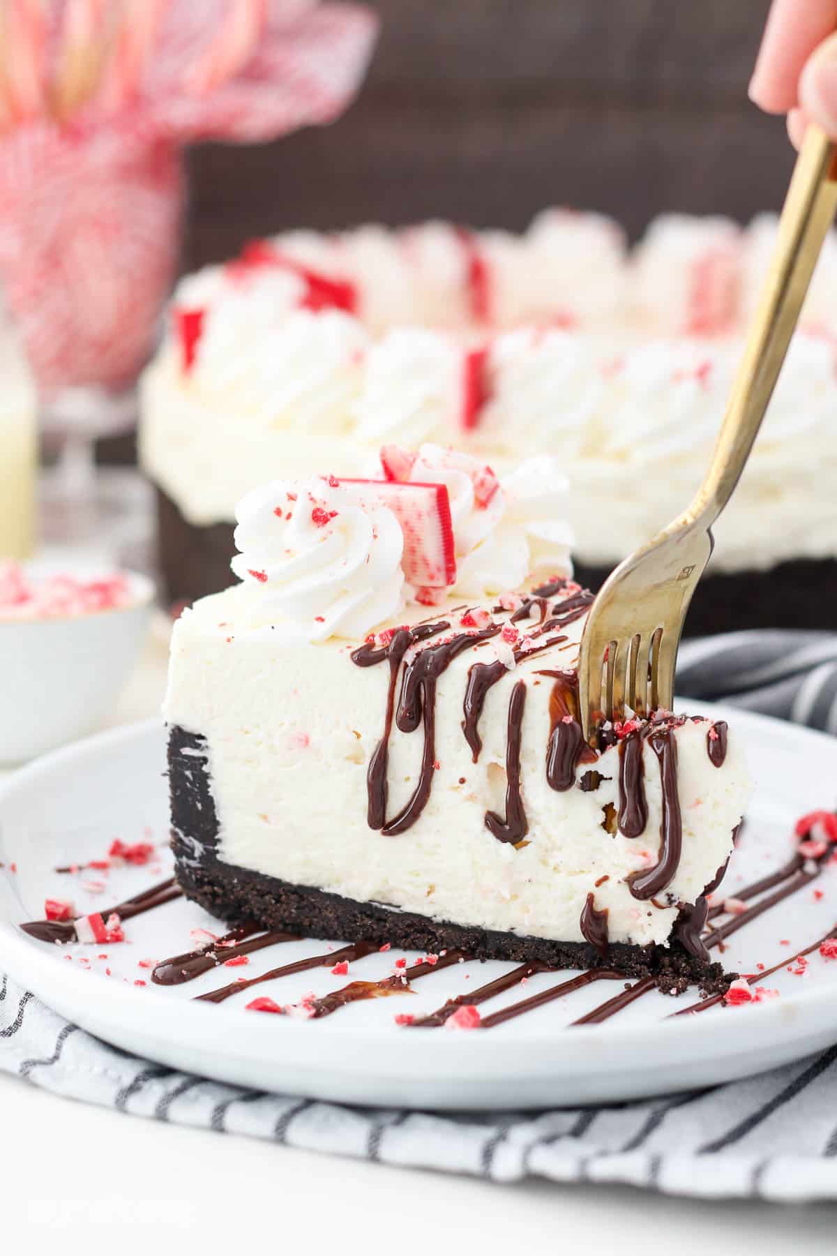 A gold fork sinking into a slice of peppermint bark cheesecake with a thick Oreo crust