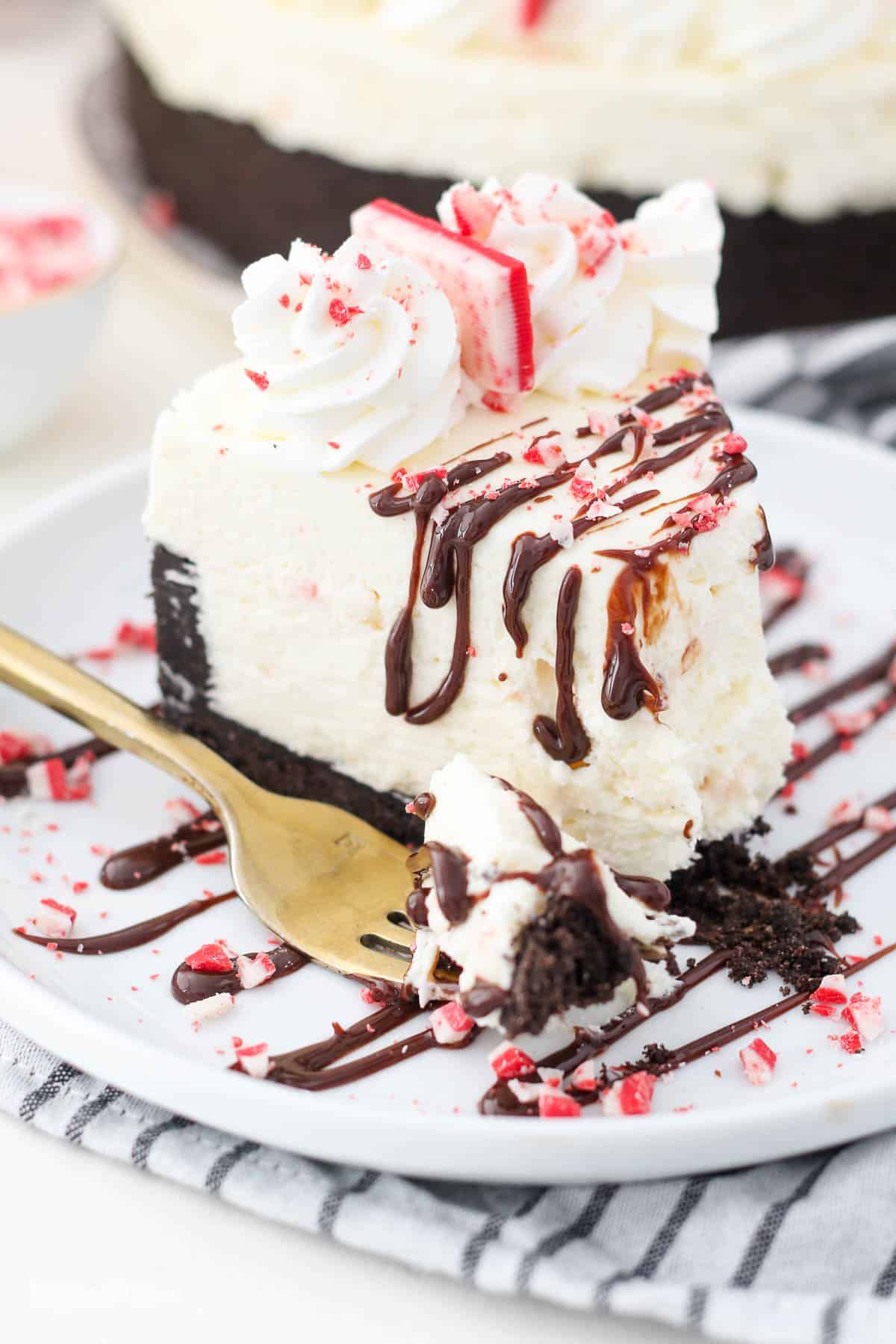 A big slice of peppermint cheesecake with a few bites taken out of it. The cheesecake is garnished with hot fudge and crushed peppermint