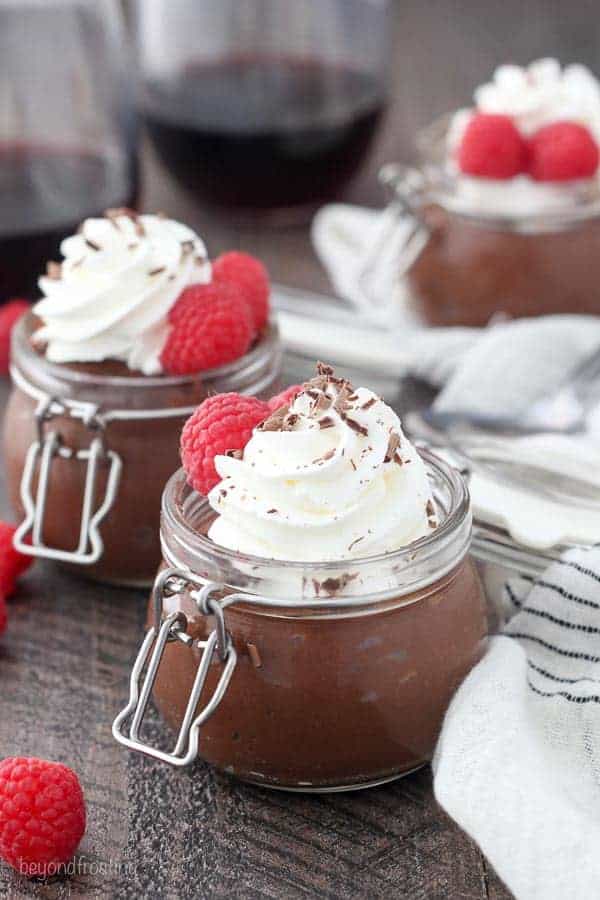 Three little jars lined up, each one is filled with chocolate pudding, a swirl of whipped cream, shaved chocolate and two raspberries