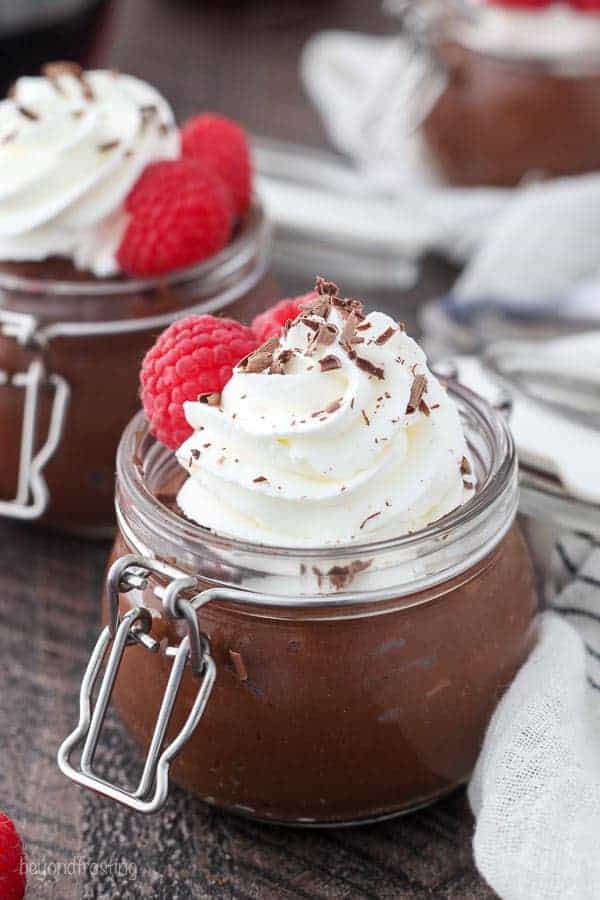 A beautiful little jar filled with chocolate pudding and topped with whipped cream and chocolate sprinkles with a couple of raspberries on the side