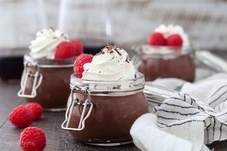 Three small jar filled with chocolate pudding topped with whipped cream and raspberries and wrapped in a thin black striped towel