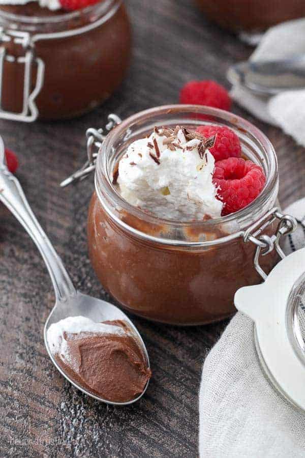 An overhead view of jar of chocolate pudding, and a silver spoon with a dollop of pudding on it