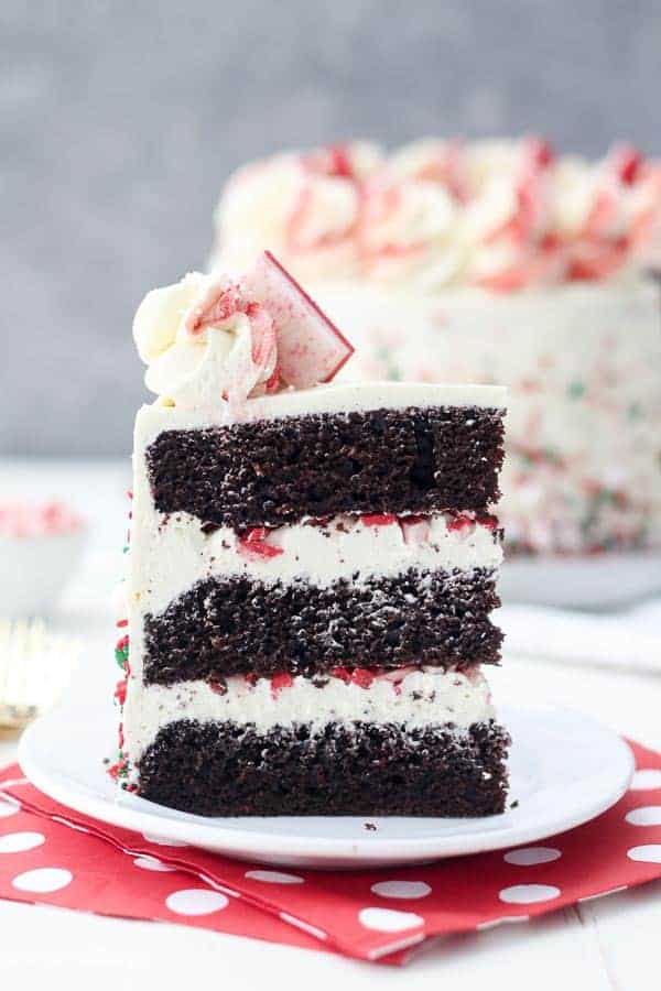 A tall slice of a 3 layer chocolate peppermint cake on a small white plate sitting on red and white polka dot napkins.