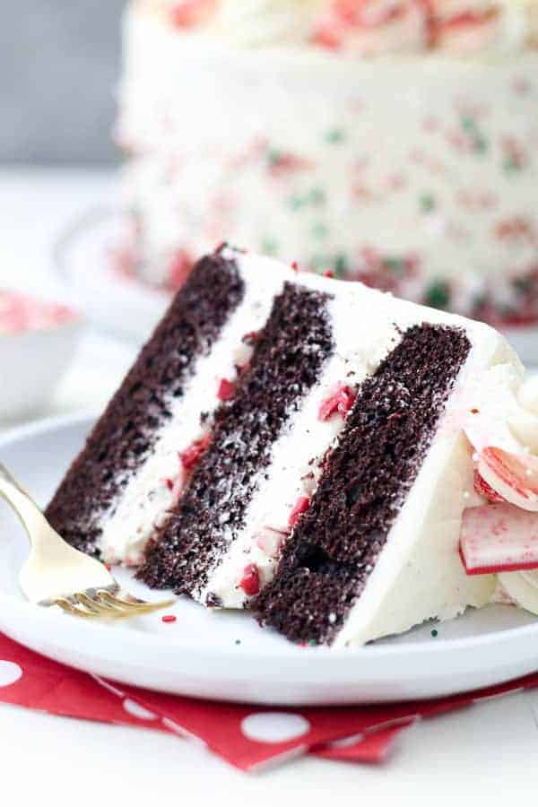 A close up of a 3 layer chocolate cake with thick layers of buttercream in between and crushed peppermint bark chocolate.