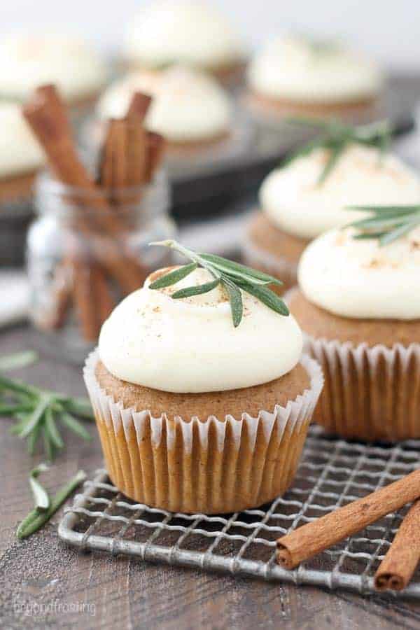 Three gingerbread cupcakes with white frosting and a rosemary garnish.