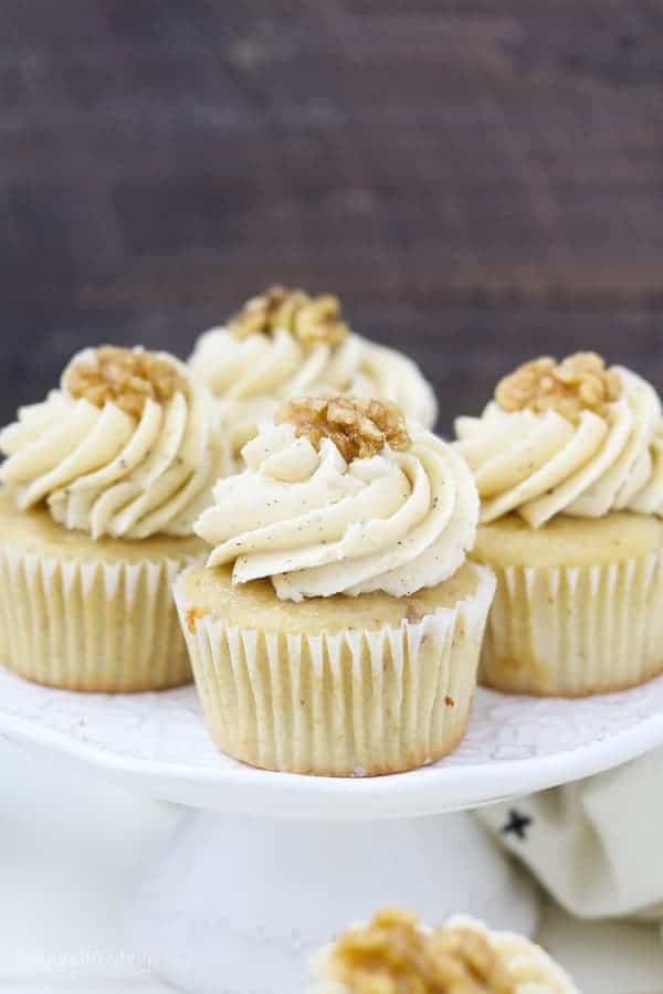 A small white cake stand with 4 cupcakes on top, each cupcake is garnished with a walnut