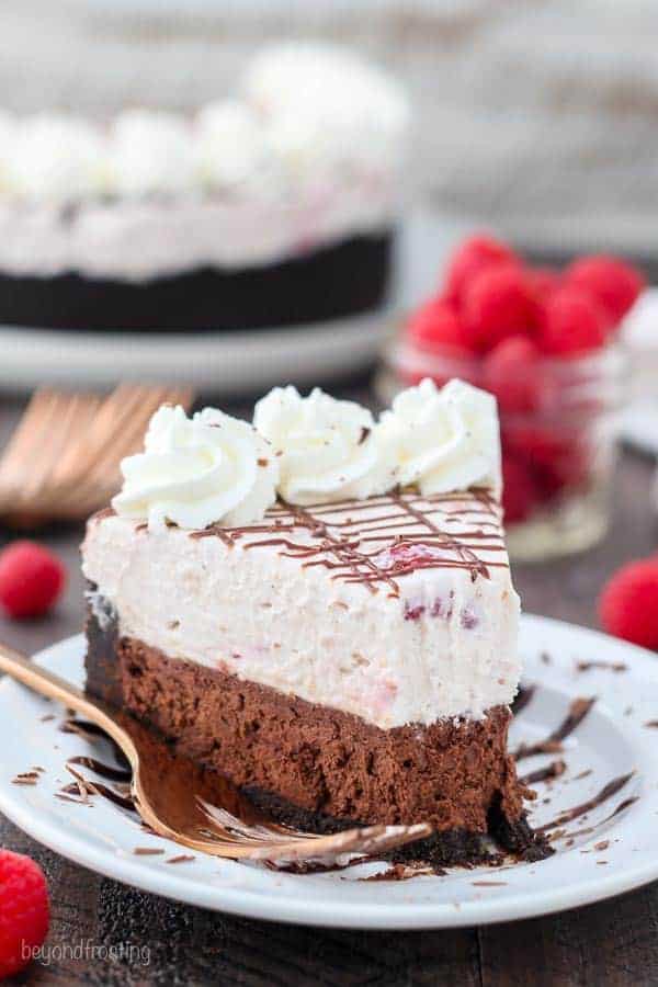 A slice of chocolate raspberry mousse cake on a white plate with a big bite taken out of the front
