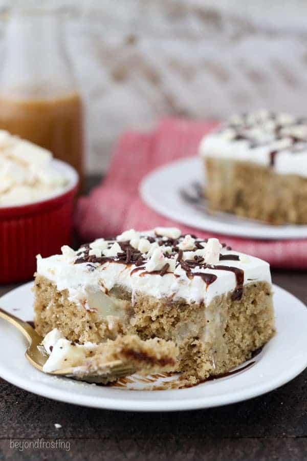 A mocha flavored cake on a white plate soak in pudding and topped with white cream. The cake has a few bites taken out of it and it's drizzled with hot fudge and sprinkled with peppermint candy.