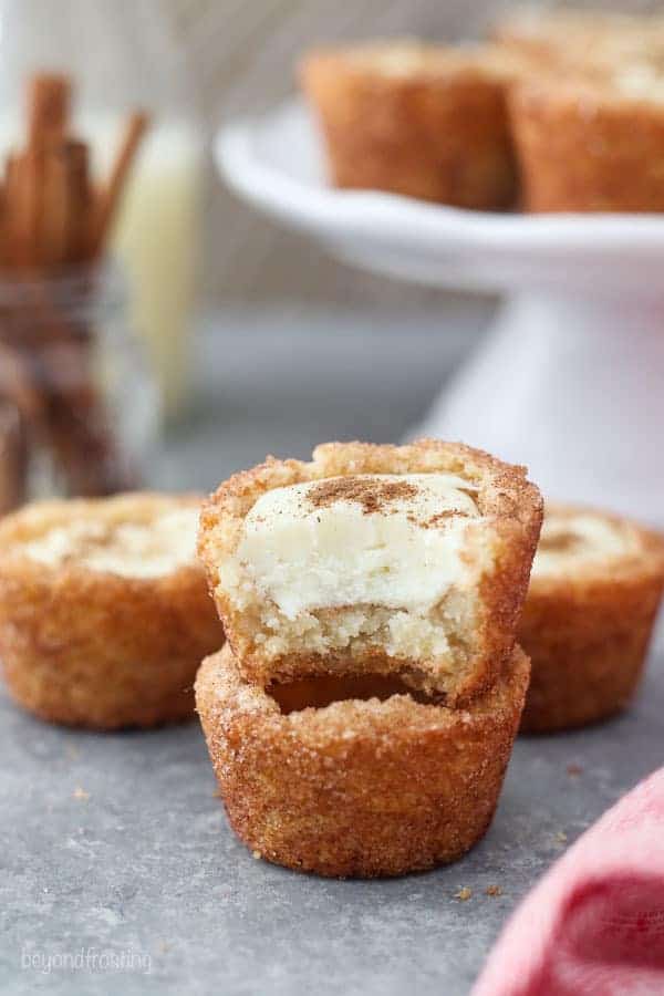 Two snickerdoodle cookie cups stacked, the cookie on top has a bite taken out of it showing the ganache filling.
