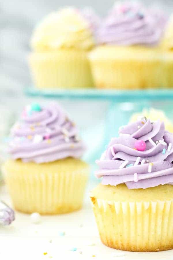 A close up shot of a pretty cupcake topped with purple Swiss Meringue buttercream and pretty sprinkles