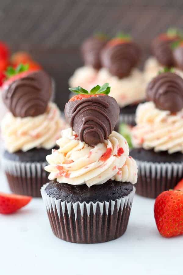 Three chocolate cupcakes covered with fresh strawberry buttercream and they're topped with a chocolate covered strawberry.
