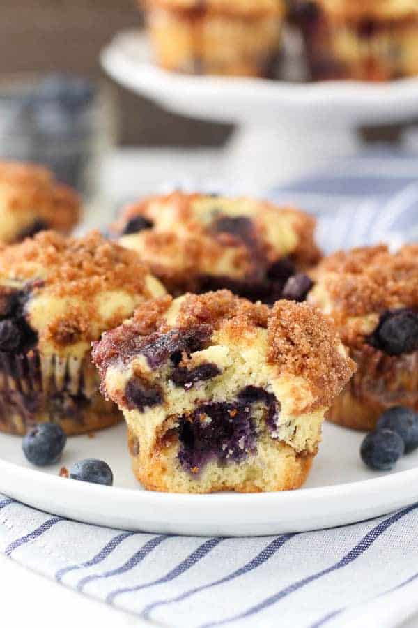 A close up shot of a blueberry muffins with a couple bites taken out of it showing the inside of the muffins, which is loaded with berries. There's a cinnamon sugar crumb topping.