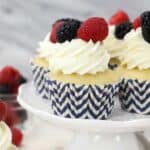 A mini white cake stand with vanilla cupcakes that have navy chevon cupcake liners and frosted with mascarpone whipped cream and garnished with berries on top