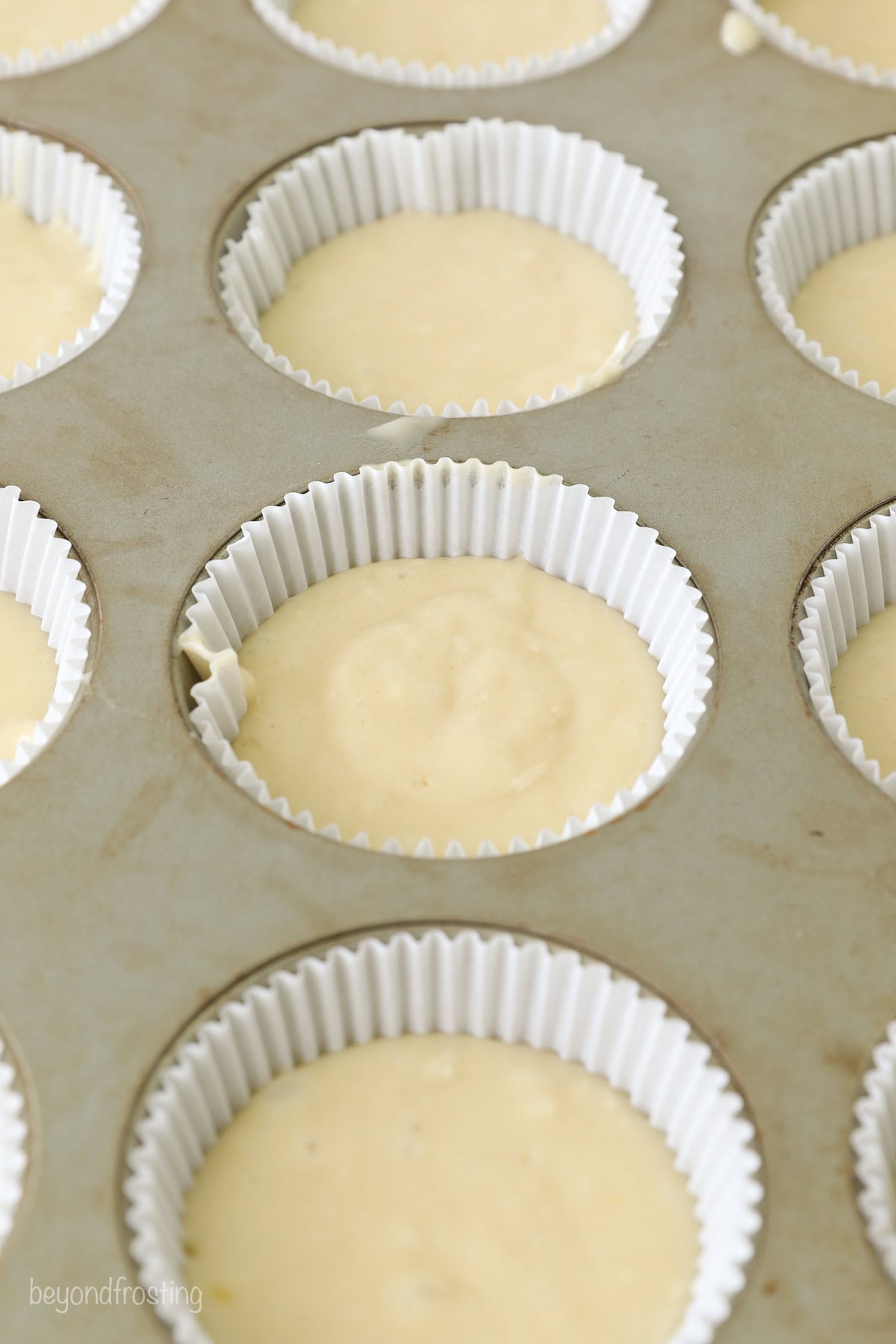 A lined cupcake pan filled with yellow cupcake batter.