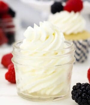 A piped swirl of mascarpone whipped cream in a glass jar, with frosted cupcakes in the bacgkround.
