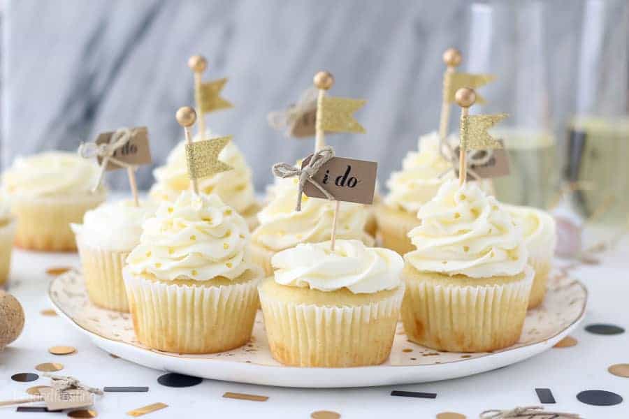 A plate of engagement themed cupcakes are super cute decorated with a buttercream rose and a little cupcake topper that says "I do" and the other ones with gold heart shaped sprinkles