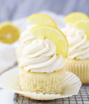 An unwrapped cupcake sitting on a wire rack with a big swirl of lemon frosting and a lemon garnish on top